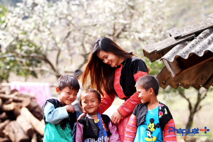 Một bạn trẻ chụp cùng những đứa trẻ vùng cao trong vườn hoa mơ nở rộ.